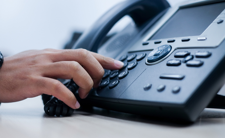 Close up of a person using a desk phone to call support