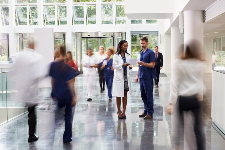 Bright hospital lobby with hospital professionals and visitors quickly passing by